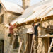 Maison ancienne en pierre en cours de rénovation thermique, avec toiture isolée et deux artisans travaillant sur une façade éclairée par le soleil.