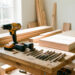 Atelier lumineux de rénovation intérieure avec une perceuse-visseuse sans fil, des batteries, des forets et des planches de bois soigneusement rangés sur un établi.