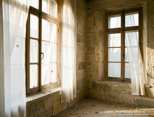 Fenêtres en bois d’une maison ancienne laissant passer de légers courants d’air qui font bouger les rideaux.