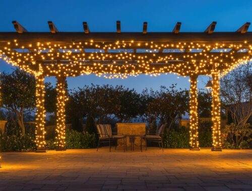 Pergola de jardin éclairée par des guirlandes lumineuses au-dessus d’une terrasse.