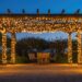 Pergola de jardin éclairée par des guirlandes lumineuses au-dessus d’une terrasse.