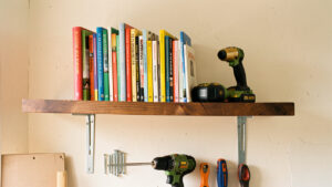 Étagère en bois lourde solidement fixée sur un mur en placo, avec des livres rangés et des outils de bricolage disposés en dessous.