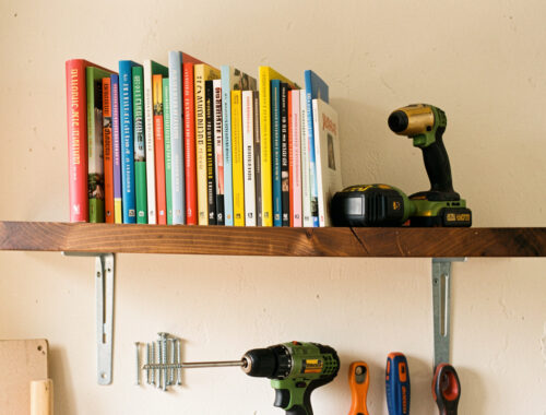 Étagère en bois lourde solidement fixée sur un mur en placo, avec des livres rangés et des outils de bricolage disposés en dessous.