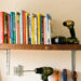 Étagère en bois lourde solidement fixée sur un mur en placo, avec des livres rangés et des outils de bricolage disposés en dessous.